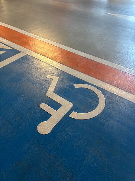 A high angle shot of a white handicapped accessibility icon painted on a bright blue concrete floor with red and white boundary lines in an indoor parking lot